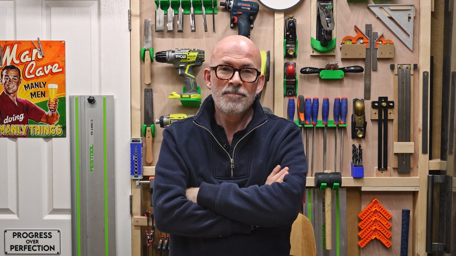 Mark standing in front of the workshop tool wall, arms folded